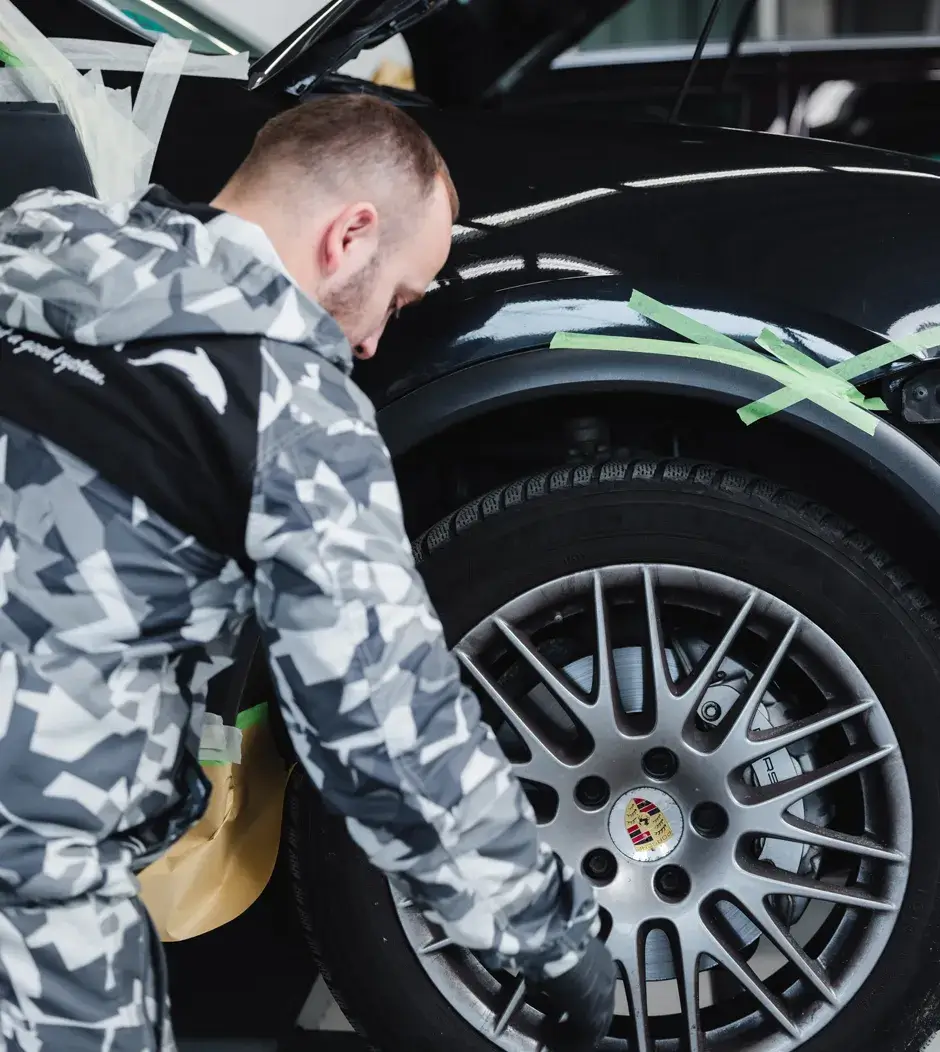 Ein Mitarbeiter von Karosserie Blanke klebt sorgfältig einen schwarzen Porsche vor der Lackierung im Radlaufbereich ab.