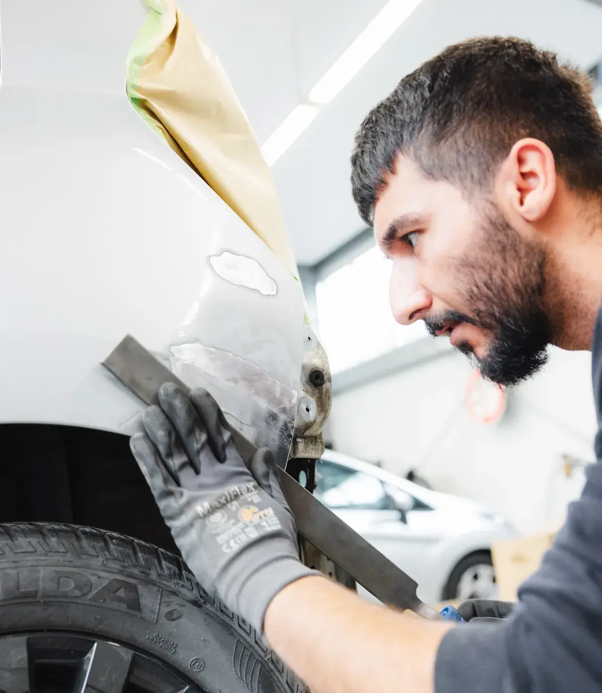 Ein Karosseriebauer bei der Feinbearbeitung eines Kotflügels mit Schleiflineal und gespachtelter Fläche - Vorbereitung für die Lackierung.